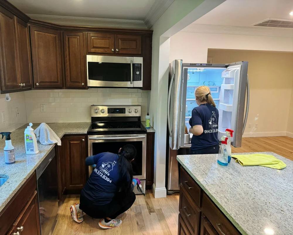 Two team members deep cleaning a kitchen oven and refrigerator